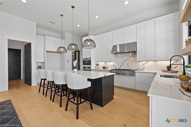 kitchen featuring stainless steel gas cooktop, a center island, white cabinetry, hanging light fixtures, and range hood