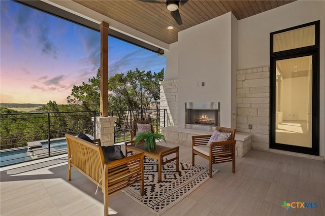 patio terrace at dusk featuring an outdoor living space with a fireplace and ceiling fan