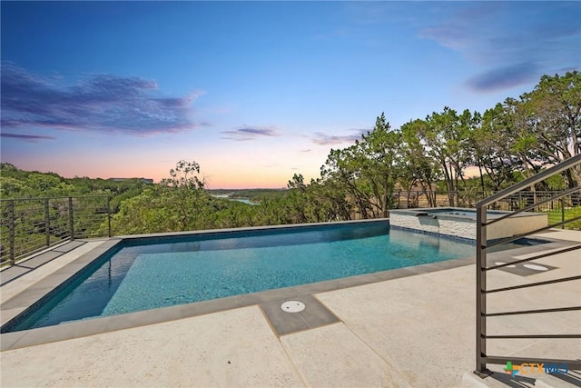 pool at dusk with an in ground hot tub