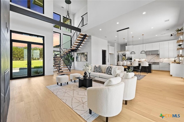 living room with light wood-type flooring, a high ceiling, and french doors