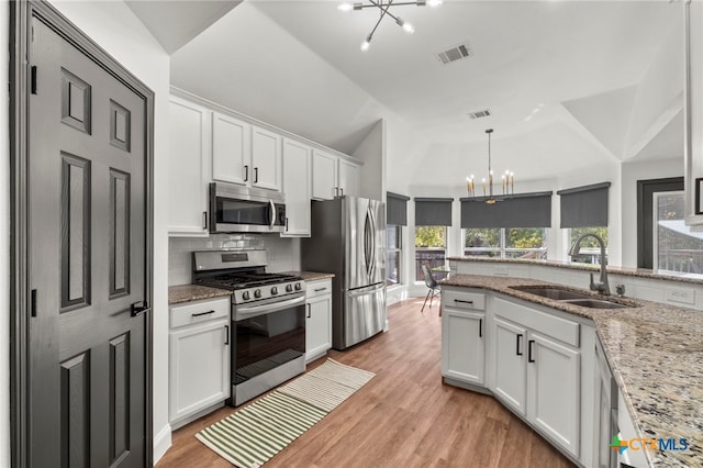 kitchen featuring stainless steel appliances, white cabinetry, sink, light stone counters, and an inviting chandelier