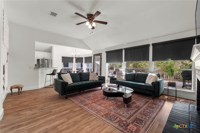 living room featuring ceiling fan with notable chandelier, hardwood / wood-style flooring, and vaulted ceiling