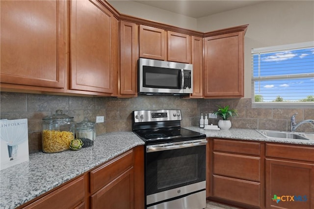 2226 Hayes St, Temple, TX 76502 - kitchen featuring appliances with stainless steel finishes, light stone counters, brown cabinetry, and tasteful backsplash