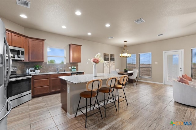 2226 Hayes St, Temple, TX 76502 - kitchen featuring appliances with stainless steel finishes, decorative backsplash, a kitchen island, brown cabinetry, and a kitchen breakfast bar