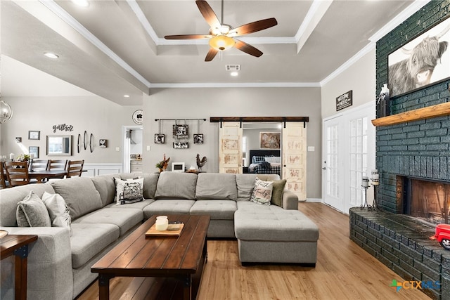 living room featuring visible vents, a raised ceiling, a ceiling fan, crown molding, and light wood-type flooring