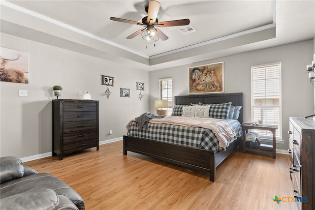 bedroom featuring light wood-style floors, a raised ceiling, visible vents, and ornamental molding