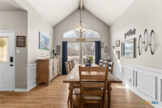 dining space with light wood-type flooring, an inviting chandelier, vaulted ceiling with beams, and a wainscoted wall