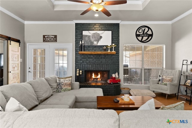 living room with a barn door, a ceiling fan, ornamental molding, wood finished floors, and a fireplace