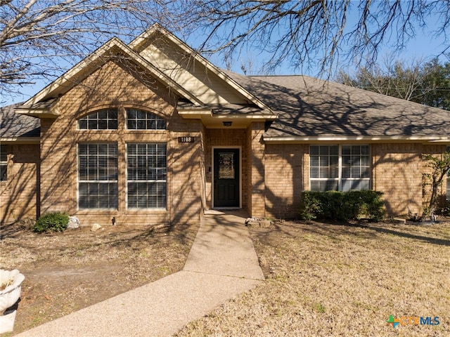 ranch-style home with a shingled roof, brick siding, and a front lawn