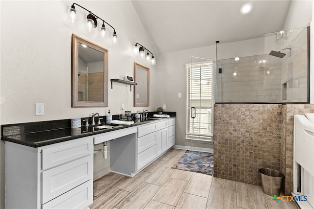 bathroom featuring lofted ceiling, double vanity, tiled shower, and a sink