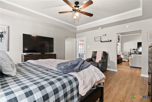 bedroom with ornamental molding, light wood-type flooring, a raised ceiling, and baseboards