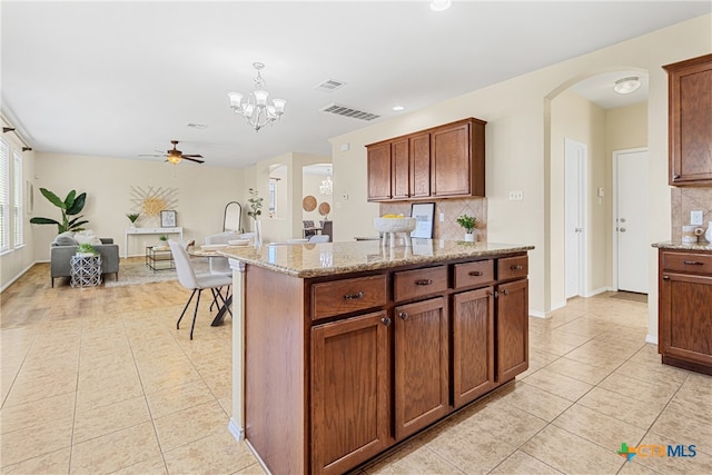 kitchen featuring light stone countertops, a center island, backsplash, light tile patterned floors, and ceiling fan with notable chandelier