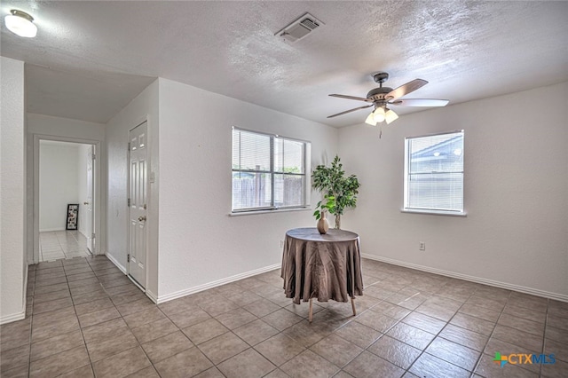 interior space with a textured ceiling, ceiling fan, and light tile patterned flooring