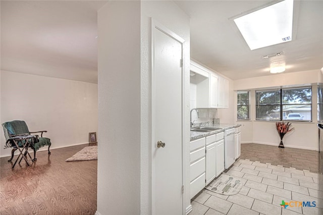 kitchen featuring white dishwasher, white cabinets, sink, a skylight, and light wood-type flooring