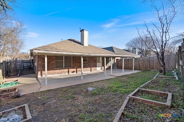 back of property featuring a patio, a fenced backyard, a garden, brick siding, and a chimney