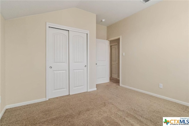 unfurnished bedroom with carpet flooring, a closet, baseboards, and vaulted ceiling