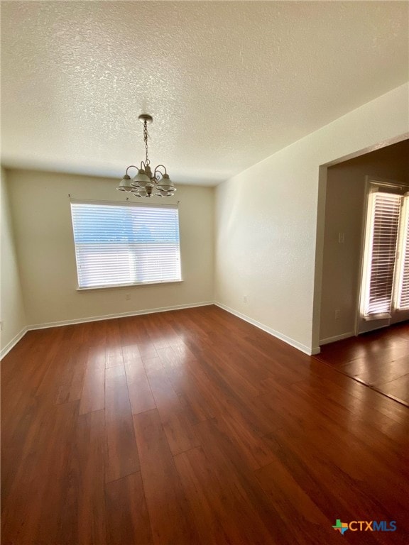 spare room featuring a textured ceiling, dark hardwood / wood-style floors, and a chandelier