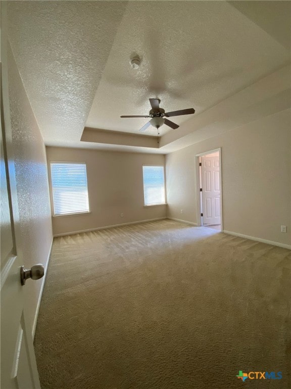 unfurnished room with ceiling fan, a textured ceiling, carpet floors, and a tray ceiling