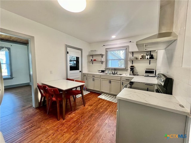 kitchen featuring dark wood-style floors, stainless steel electric range oven, wall chimney exhaust hood, open shelves, and a sink