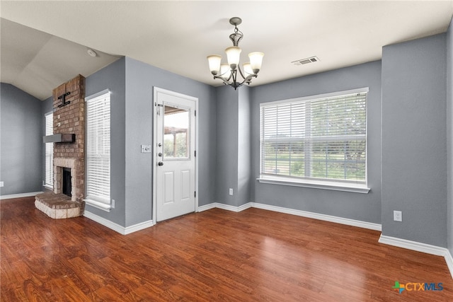interior space with wood finished floors, an inviting chandelier, baseboards, a brick fireplace, and visible vents
