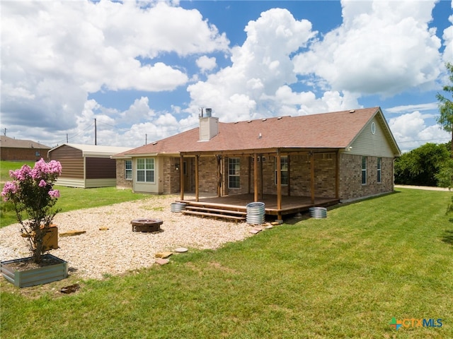 rear view of house featuring a lawn, a wooden deck, brick siding, and an outdoor fire pit