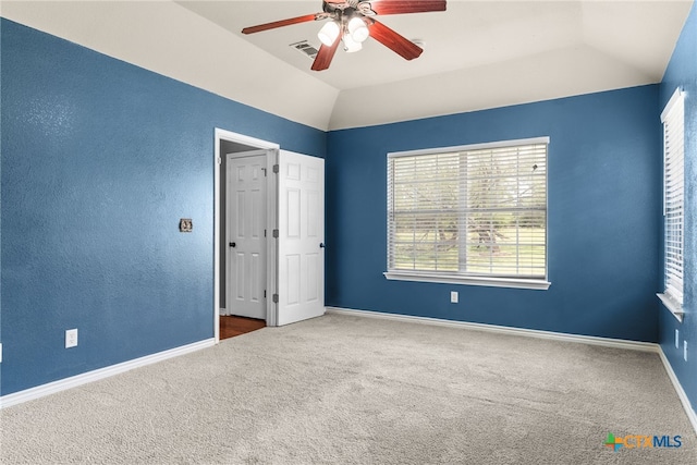 unfurnished bedroom featuring carpet flooring, vaulted ceiling, visible vents, baseboards, and ceiling fan