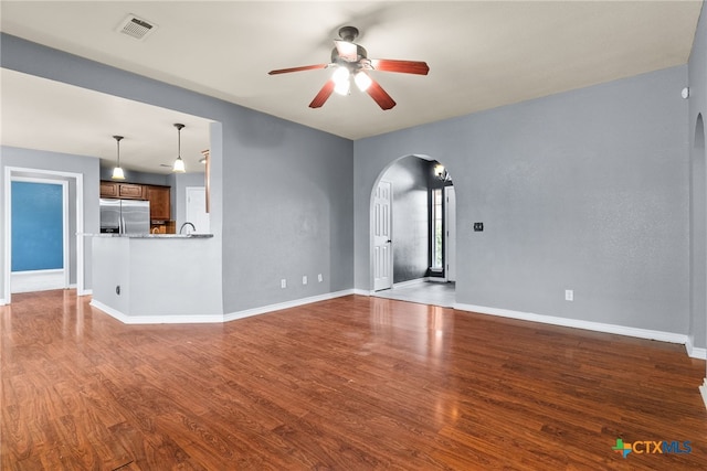 unfurnished living room featuring arched walkways, wood finished floors, visible vents, and a ceiling fan
