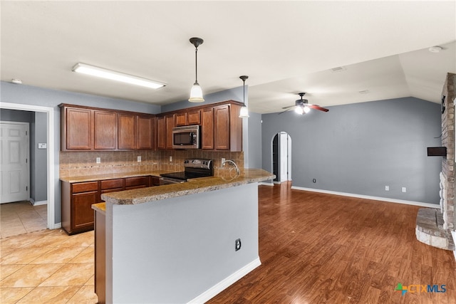 kitchen featuring a peninsula, arched walkways, tasteful backsplash, a ceiling fan, and appliances with stainless steel finishes