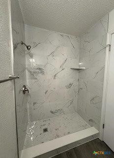 bathroom with a textured ceiling and a tile shower