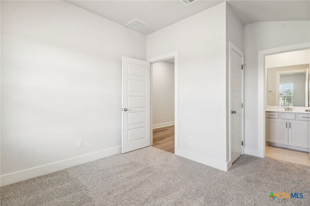 unfurnished bedroom featuring sink, light colored carpet, vaulted ceiling, and ensuite bathroom