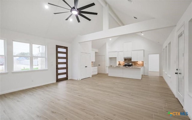 223 River Tree Dr, Palacios, TX 77465 - unfurnished living room featuring high vaulted ceiling, beamed ceiling, ceiling fan, light wood-style flooring, and baseboards