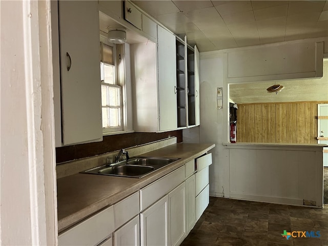 kitchen with wooden walls, sink, and white cabinetry