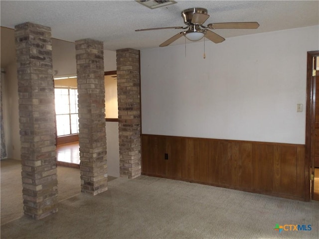 carpeted empty room featuring a textured ceiling, wainscoting, decorative columns, and wooden walls