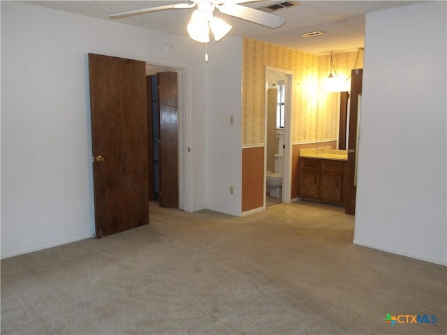 unfurnished bedroom featuring carpet floors, visible vents, a ceiling fan, ensuite bath, and wallpapered walls