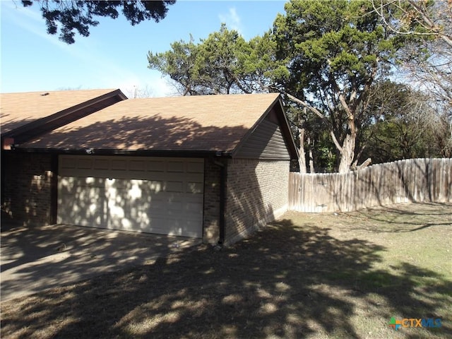 view of side of home featuring a garage, brick siding, and fence