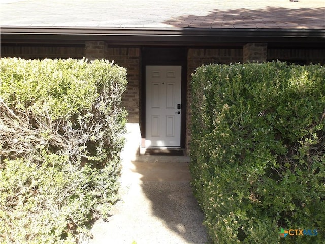 property entrance with brick siding and roof with shingles