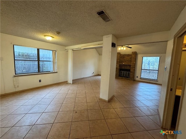 unfurnished living room with a fireplace, visible vents, a wealth of natural light, and tile patterned floors