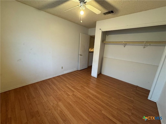 unfurnished bedroom featuring a closet, visible vents, ceiling fan, a textured ceiling, and wood finished floors