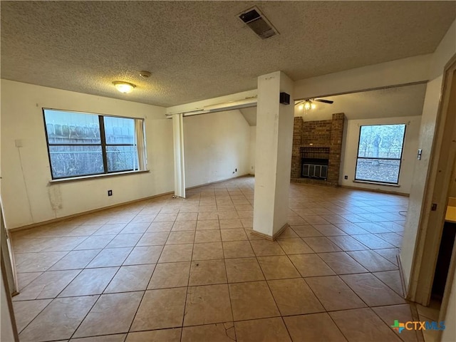 spare room featuring light tile patterned floors, visible vents, a ceiling fan, a brick fireplace, and plenty of natural light