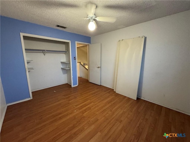 unfurnished bedroom with a closet, visible vents, a ceiling fan, a textured ceiling, and wood finished floors