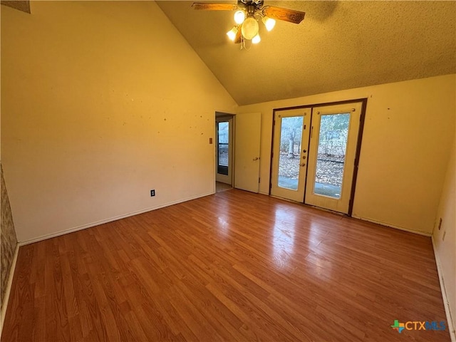 unfurnished room with high vaulted ceiling, wood finished floors, a ceiling fan, baseboards, and french doors