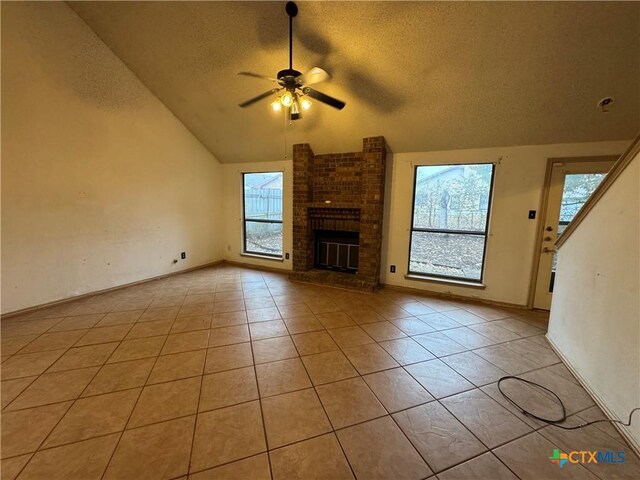 unfurnished living room featuring light tile patterned floors, ceiling fan, vaulted ceiling, a textured ceiling, and a brick fireplace