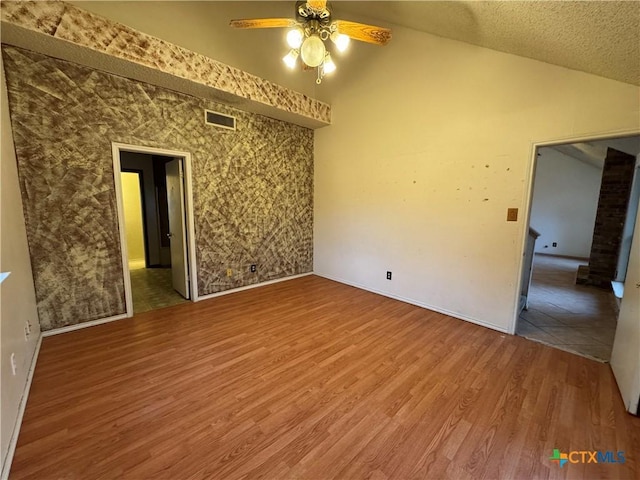 unfurnished room with visible vents, a ceiling fan, vaulted ceiling, a textured ceiling, and wood finished floors