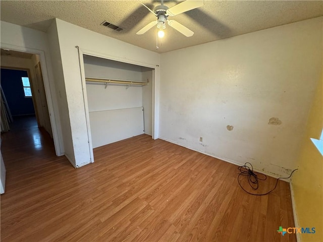 unfurnished bedroom featuring light wood finished floors, visible vents, a ceiling fan, a textured ceiling, and a closet