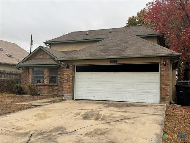 view of front facade featuring a garage, fence, concrete driveway, and roof with shingles