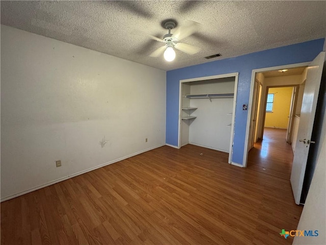 unfurnished bedroom with a closet, visible vents, ceiling fan, a textured ceiling, and wood finished floors