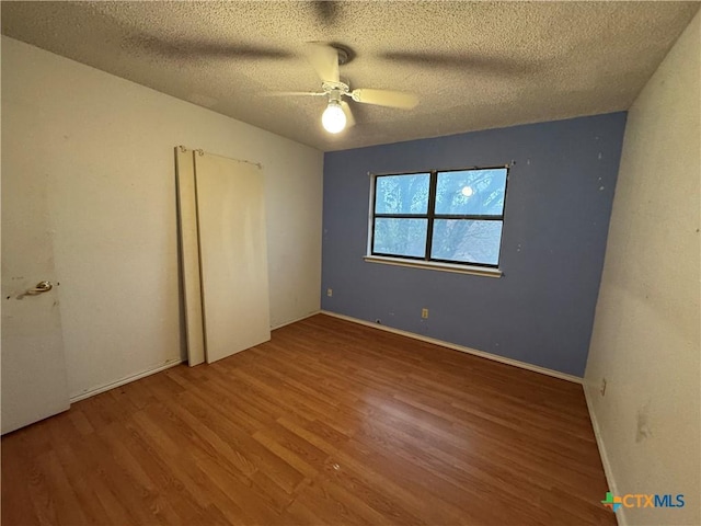 unfurnished bedroom with a textured ceiling, ceiling fan, wood finished floors, and baseboards