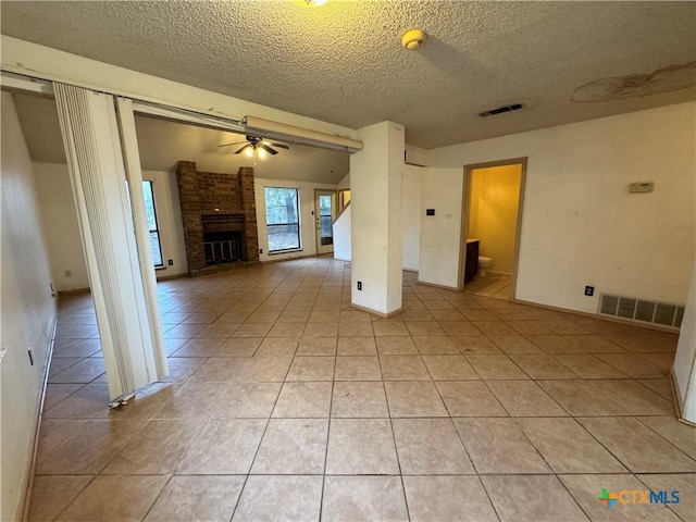 unfurnished living room featuring a brick fireplace, ceiling fan, visible vents, and light tile patterned flooring