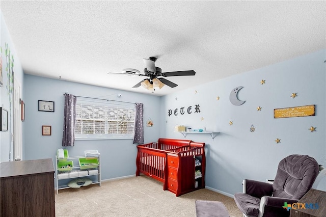 carpeted bedroom featuring baseboards, a textured ceiling, ceiling fan, and a nursery area