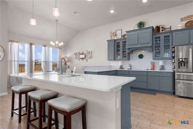 kitchen with a kitchen island with sink, stainless steel fridge with ice dispenser, pendant lighting, and tasteful backsplash